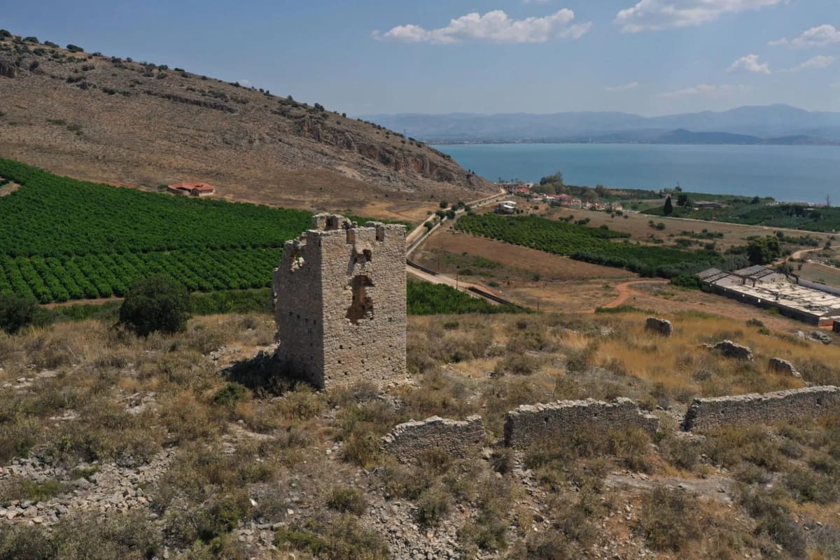 The ruined stone Tower of the Princess with its court wall, orange groves below and the Argolic Gulf beyond